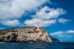 Thumbnail for an image displaying: A view of a lighthouse at the end of Capri, taken from the ocean.