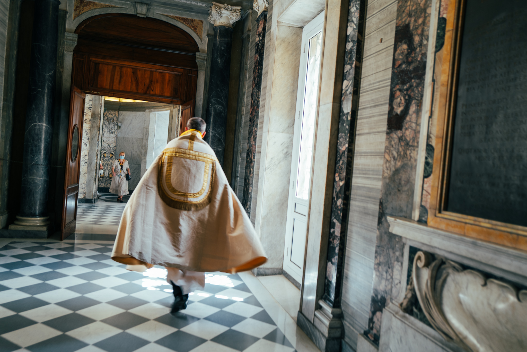 A bishop hurries through St. Peter's Basilica, as a woman wearing a surgical mask watches.